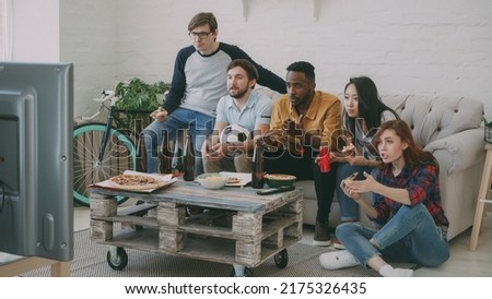 Multi-ethnic group of friends sports fans watching football championship on TV together eating pizza and drinking beer at home indoors
