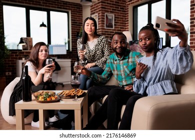 Multiethnic Group Of Friends Taking Selfie Photo Together While At Wine Party In Living Room. Happy Smiling Adults At Home Enjoying Time Together While Drinking Alcoholic Beverages And Taking Pictures