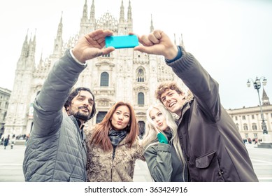 Multi-ethnic group of friends taking a selfie in front of a famous landmark - Tourists photographing the Duomo cathedral in Milan - Four people on vacation sightseeing the city