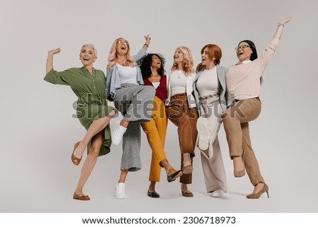 Multi-ethnic group of happy mature women embracing and dancing against grey background