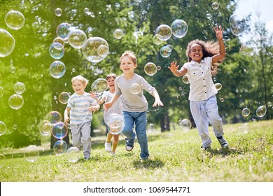 Multi-ethnic group of little friends with toothy smiles on their faces enjoying warm sunny day while participating in soap bubbles show