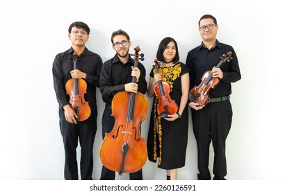 multiethnic group of musicians, string quartet posing for camera not playing. three men and a girl mixed group of musicians with wooden string instruments, standing against a white wall - Shutterstock ID 2260126591