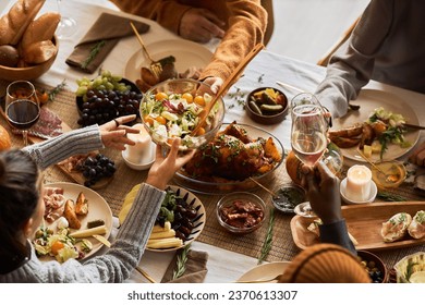 Multiethnic group of people at festive dinner table celebrating Thanksgiving together and enjoying rustic roasted dishes, copy space