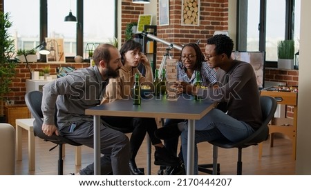 Multiethnic group of people having fun with tower pieces, playing board games with square building and wooden blocks on table. Friends laughing and enjoying leisure pasttime activity.