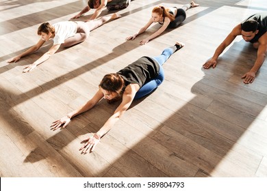 Multiethnic group of people lying and doing stretching exercises on the floor in yoga studio