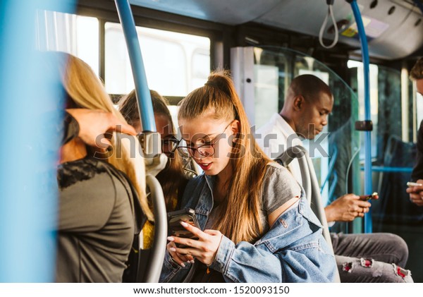 A multi-ethnic group of people in public\
transport and all use a mobile\
phone