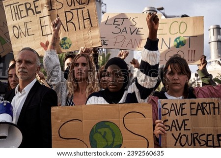 Multiethnic group of people at a refinery protesting against global warming, raising fist in favor of saving the planet earth.