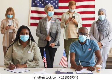 Multi-ethnic group of people standing in row and wearing masks at polling station on election day, focus on African-American couple looking at camera while registering for voting