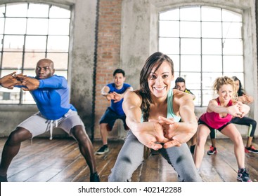 Multi-ethnic group of people training in a gym - Trainer and sportive persons doing squats in a fitness class