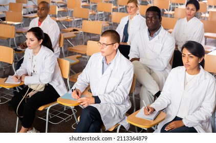 Multiethnic Group Of People In White Lab Coats Listening Carefully And Making Notes During Professional Training For Health Workers