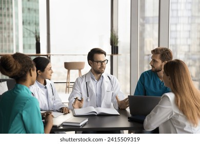 Multiethnic group of practitioners discussing collaboration, medical occupation, career in medicine at meeting in hospital office,. Leader of diverse medical team talking to positive doctors at table - Powered by Shutterstock