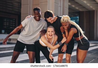 Multi-ethnic Group Of Runners Standing Together After Exercising Session Outdoors And Smiling. Group Of Men And Women In Sportswear Standing Together And Laughing After Workout Training.