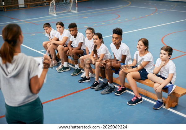 Multi-ethnic\
group of school kids listening to their sports teacher during\
physical education class at school\
gym.
