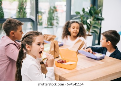 Multiethnic Group Of Schoolkids Eating Lunch While Sitting Together At Table 