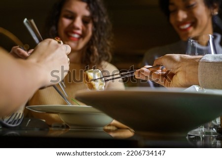 Multiethnic group of smiling young friends eating dim sum dumplings at fusion bar restaurant - close up on the chopsticks picking the food - food and drink, people lifestyle concept