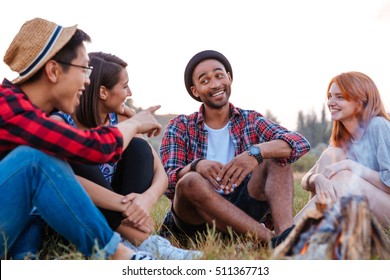 Multiethnic Group Of Smiling Young People Sitting And Talking Near Bonfire