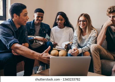 Multi-ethnic group of students learning on line together with a computer at college campus. Man showing something interesting to classmates on laptop.