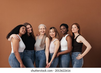 Multi-ethnic group of women of different ages posing against brown background looking at camera