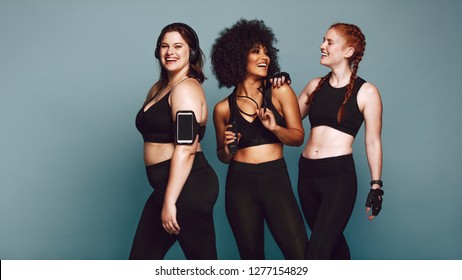 Multi-ethnic Group Of Women Together Against Grey Background And Smiling. Diverse Group Females In Sportswear After Workout.