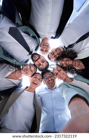 Multiethnic group of work colleagues embraced in circle, face down taking a selfie smiling and looking at the camera. Vertical image, POV business people doing team building. 