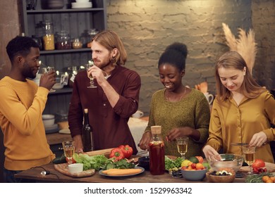 Multi-ethnic Group Of Young People Cooking Dinner Together Standing At Table In Modern Interior And Chatting