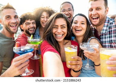 Multi-ethnic group of young people drinking cocktails outside at sunset - Happy friends taking selfie holding drinks glasses at summer party - Summertime vacations with guys and girls having fun  - Powered by Shutterstock