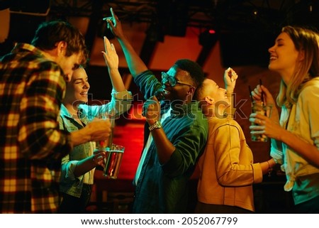 Multi-ethnic group of young people having fun and singing karaoke in a bar at night. Focus is on black man. 