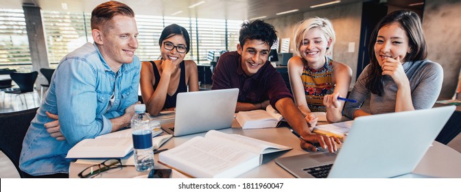 Multiethnic group of young people studying together at a table looking at laptop. Young students in cooperation with their school assignment. - Powered by Shutterstock