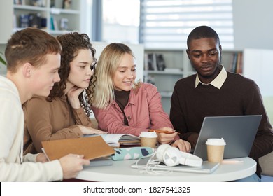 Multi-ethnic group of young people studying together while sitting at table in college library and looking at laptop screen - Shutterstock ID 1827541325