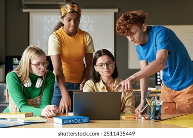Multiethnic group of young students using laptop with female teacher in class and pointing at computer screen