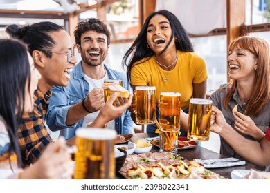 Multiethnic happy friends drinking beer glasses sitting at brewery pub restaurant table - Smiling guys and girls having fun at rooftop dinner party - Food and beverage lifestyle  - Powered by Shutterstock