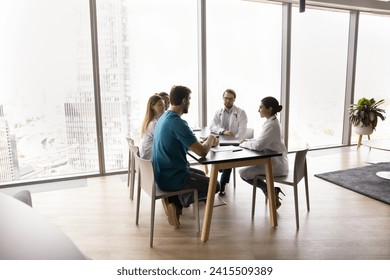 Multiethnic hospital staff of young doctors talking at table, meeting for teamwork in large clinic office hall space with large window, discussing profession, collaboration, consulting colleagues - Powered by Shutterstock
