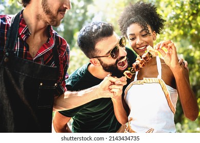 Multiethnic Joyful young people joking outdoors at barbecue eating meat skewers and having fun carefree together - Friends carefree on weekend grilling together in thecountryside - Shutterstock ID 2143434735