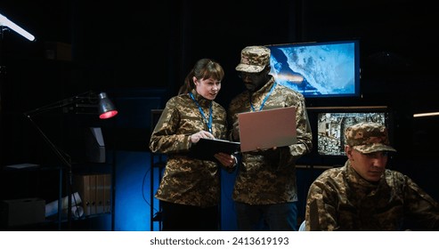 Multiethnic male and female army officials standing in monitoring room and discussing war operation strategy. Caucasian woman with tablet device and African American man with laptop computer. - Powered by Shutterstock