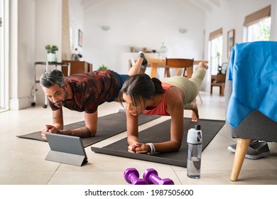 Multiethnic Mature Couple Exercising At Home And Watching Training Videos On Digital Tablet. Middle Aged Woman And Fit Indian Man Doing Planks While Watching Fitness Lessons Online On Digital Tablet.