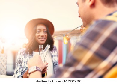 Multi-ethnic Millenial Couple Flirting While Having A Drink On Rooftop Patio At Sunset