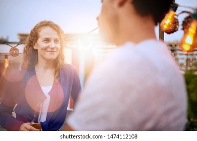 Multi-ethnic Millenial Couple Flirting While Having A Drink On Rooftop Patio At Sunset