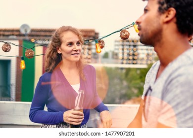 Multi-ethnic Millenial Couple Flirting While Having A Drink On Rooftop Patio At Sunset