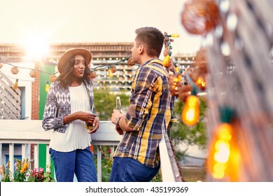 Multi-ethnic Millenial Couple Flirting While Having A Drink On Rooftop Terrasse At Sunset