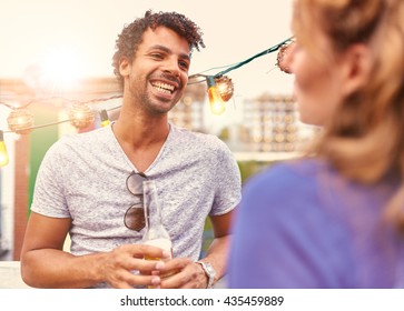 Multi-ethnic Millenial Couple Flirting While Having A Drink On Rooftop Terrasse At Sunset