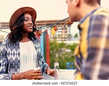 Multi-ethnic Millenial Couple Flirting While Having A Drink On Rooftop Terrasse At Sunset