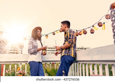 Multi-ethnic Millenial Couple Flirting While Having A Drink On Rooftop Terrasse At Sunset