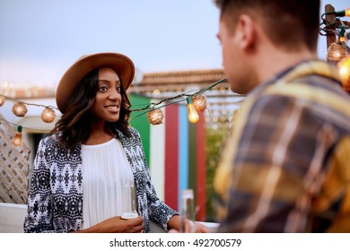 Multi-ethnic Millenial Couple Flirting While Having A Drink On Rooftop Patio At Sunset