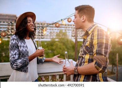 Multi-ethnic Millenial Couple Flirting While Having A Drink On Rooftop Patio At Sunset