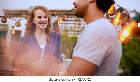 Multi-ethnic Millenial Couple Flirting While Having A Drink On Rooftop Patio At Sunset