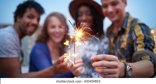 Multi-ethnic Millenial Group Of Friendsfolding Sparklers On Rooftop Terrasse At Sunset