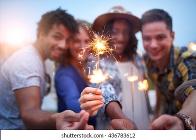 Multi-ethnic Millenial Group Of Friendsfolding Sparklers On Rooftop Terrasse At Sunset