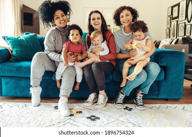 Multi-ethnic mommies sitting with children. Young mothers with babies sitting on sofa and looking at camera.