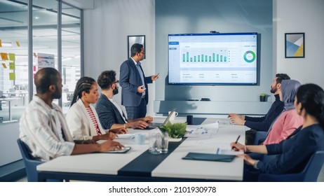 Multi-Ethnic Office Conference Room. Brilliant Indian Male CEO Does Presentation For Multi-Ethnic Group Of Managers Talking, Using TV Infographics, Statistics, Graphs. Innovative Businesspeople