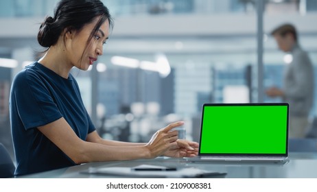 Multiethnic Office Meeting Room: Creative Asian Entrepreneur Female Use Laptop and Pointing on Green Screen Mock Up Display. - Powered by Shutterstock